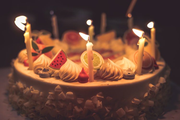 tips on cake decorating with fruit, lit candles on white cake with fruit candy shapes
