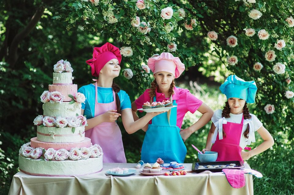 three girls wearing colorful aprons show off their cake decorating skills