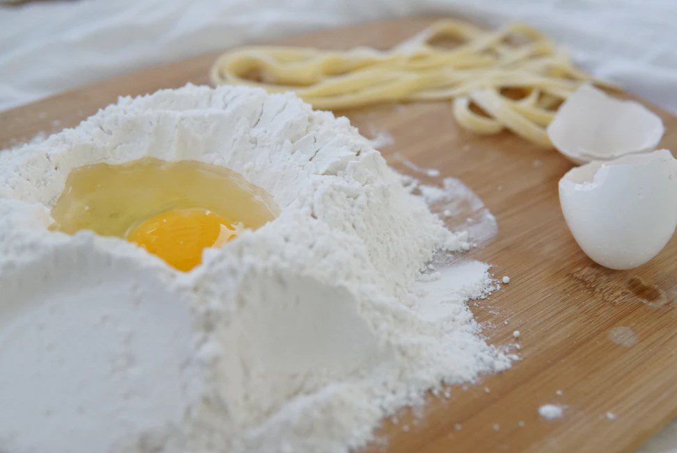 flour and eggs with eggshells on a cutting board for making noodles