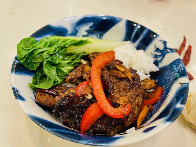 cooked Hunan beef, peppers, and bok choy in bowl with rice