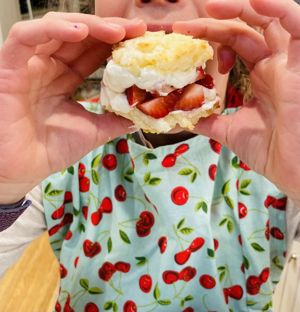 child holding fresh strawberry shortcake with whipped cream