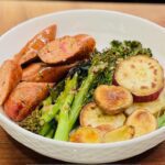 Roasted chicken sausage, broccolini, sweet potatoes in white bowl.