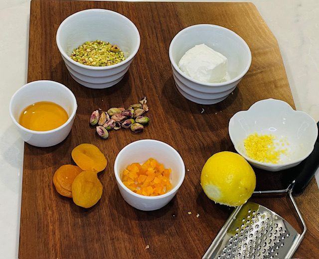 Ground pistachios, apricots, lemon, and goat cheese on cutting board.