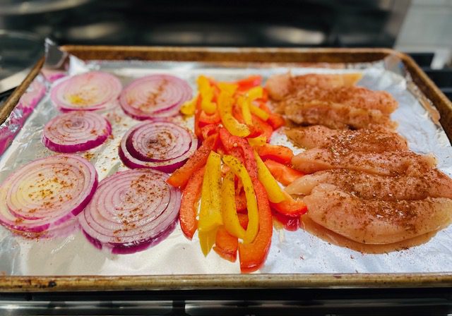 sliced red onion, yellow and red peppers, chicken tenderloins on foil lined baking sheet