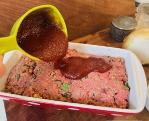 ketchup and steak sauce poured over meatloaf in loaf pan