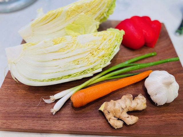 Napa cabbage, green onions, carrot and bell pepper on cutting board