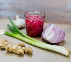 red onion, red onion slices in jar, green onions, ginger, garlic on cutting board