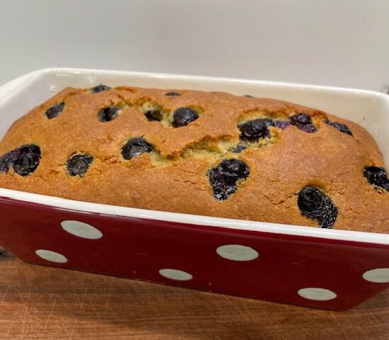 loaf of cooked blueberry banana bread cooling in red polka dot pan