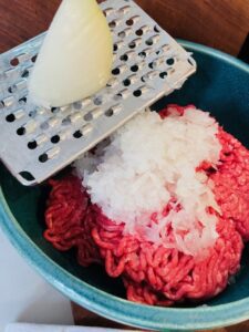 onion grated by cheese grater into bowl of ground beef for easy meatloaf recipe
