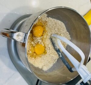 two eggs in mixing bowl of electric mixer filled with flour