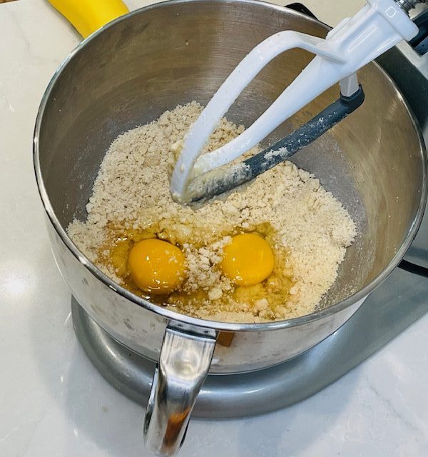 two eggs in mixing bowl of electric mixer filled with flour