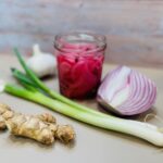 pickled red onions in a jar on cutting board with aromatics