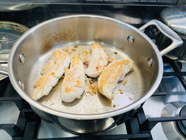 4 chicken breast tenderloins cooking in silver skillet.